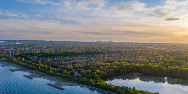 A scenic aerial view of a lakeside town with greenery and a calm water body at sunset.