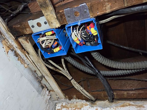 Electrical wiring in blue junction boxes under a ceiling.