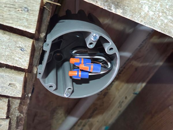 Electrical junction box with wire connectors inside wooden framing.