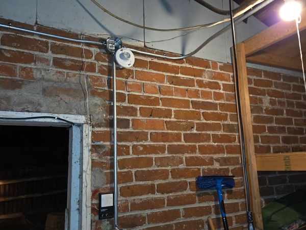 Brick wall with electrical wiring and a broom.