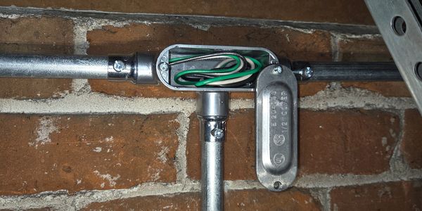 Metal conduit junction box with wiring inside on a brick wall.