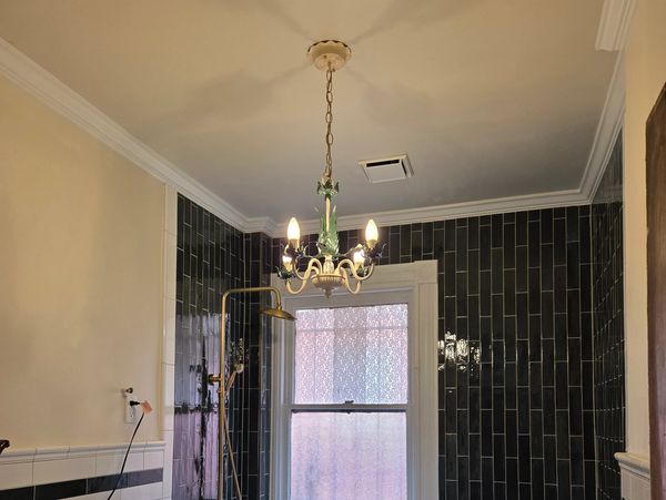 Bathroom with black tiled walls and chandelier lighting.