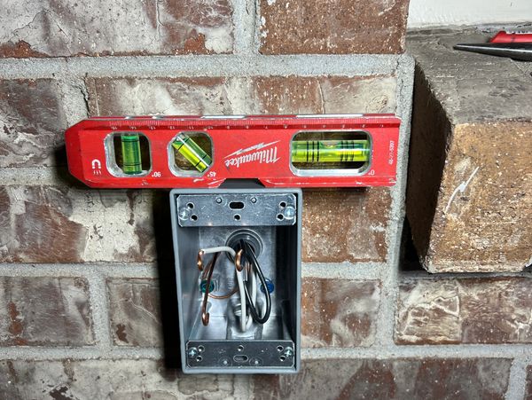 Red level tool on a metal electrical box mounted on a brick wall.