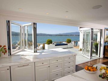 white kitchen with Bi-fold door and bi-fold servery window leading onto deck overlooking the ocean