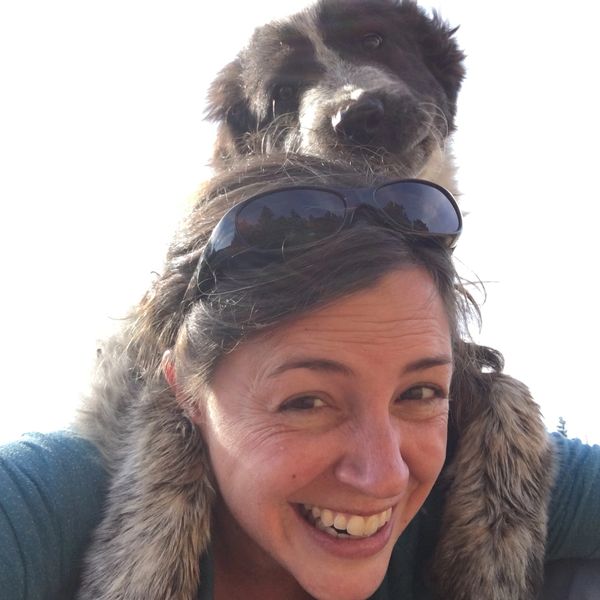 A woman smiling with a dog resting its head on her shoulders.