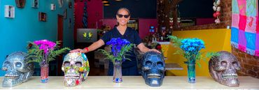 Woman standing behind a table with decorated skulls and flowers.