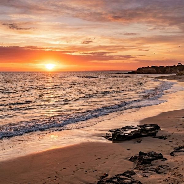 Sunset over a tranquil beach with gentle waves and rocky shore.