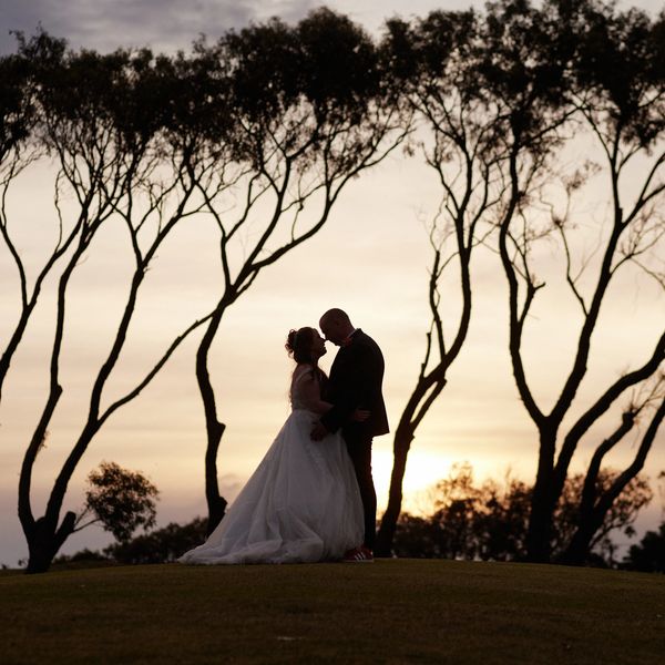 Silhouetted couple in wedding attire at sunset among trees.