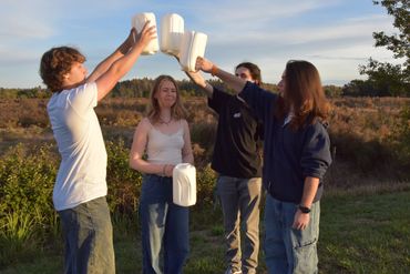 Four friends outdoors holding up empty milk jugs in a celebratory gesture.
