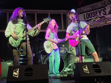 Three young musicians perform energetically on stage at Loosey's venue.