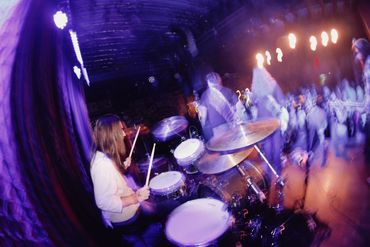 Drummer performing energetically on stage with dynamic lighting and motion blur.