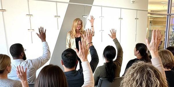 A woman leads a seminar with attendees raising their hands.