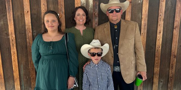 A family dressed in western attire poses against a wooden wall.