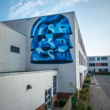 Large blue abstract mural of a helmet on a school building's wall.