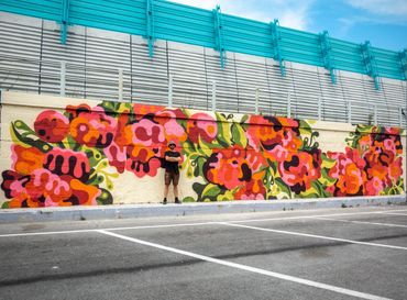 Man standing in front of a vibrant floral mural on a wall.