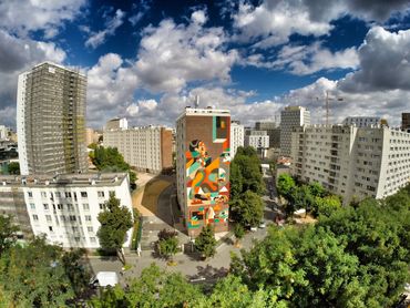 Urban buildings with a colorful mural under a partly cloudy sky.