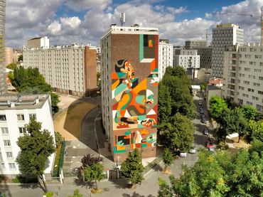 Urban buildings with a colorful mural under a partly cloudy sky.