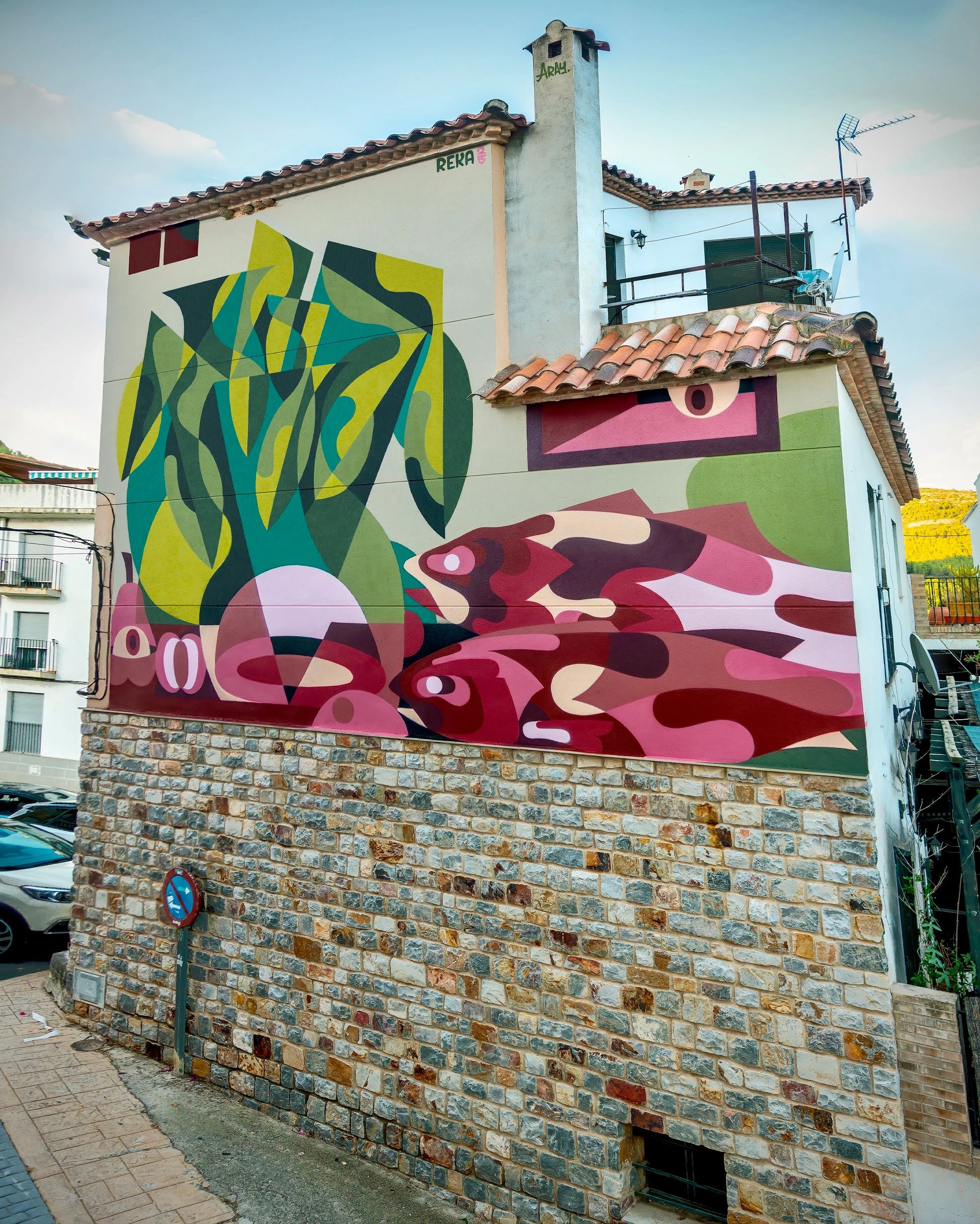 Colorful abstract mural featuring fish on a stone and white building wall.