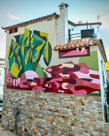 Colorful abstract mural featuring fish on a stone and white building wall.