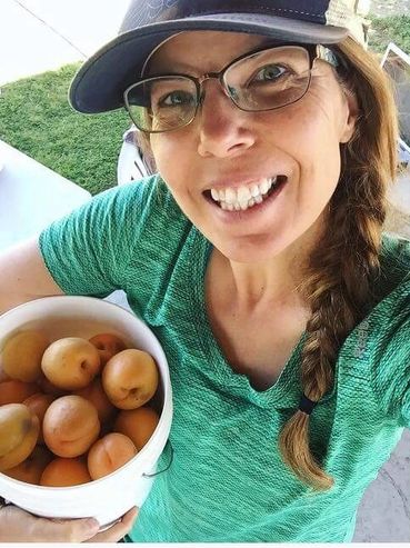 A woman smiling with a bucket of pluots.