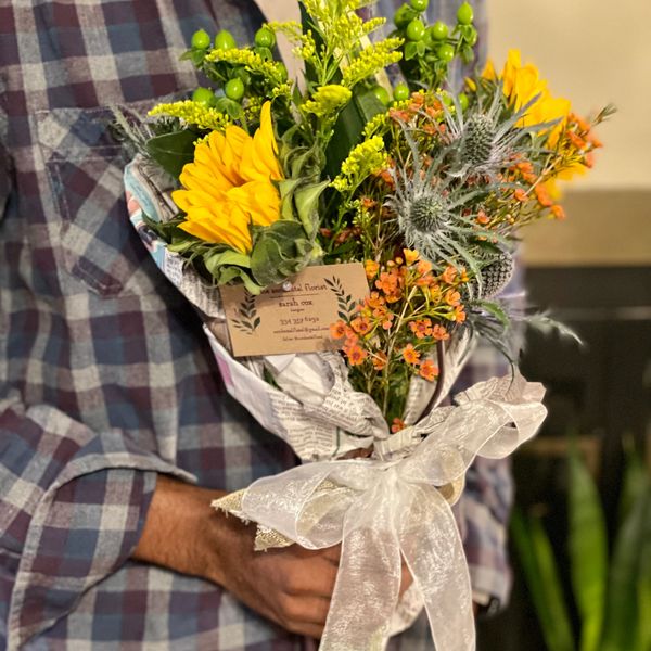 Man holding a beautiful bouquet of yellow orange and green flowers.