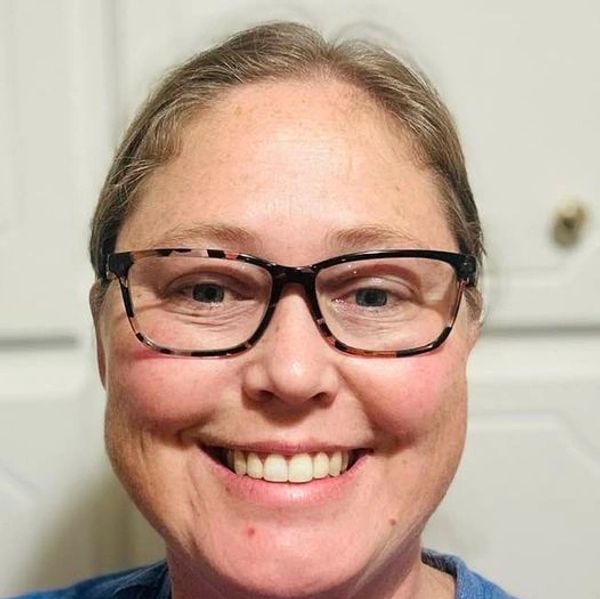 Smiling woman wearing tortoiseshell glasses against a light background.