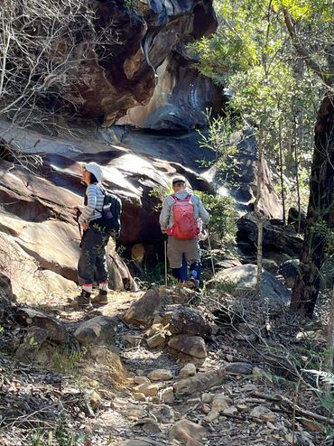 Two hikers explore a rocky forest trail on a sunny day.