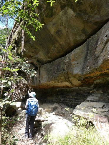 Hiker exploring a rocky overhang in a forested area.