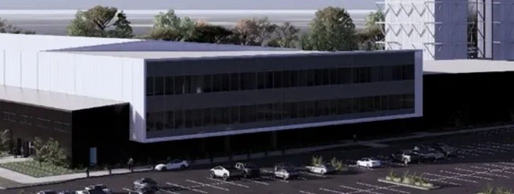 Modern office building with parking lot and trees in the background.