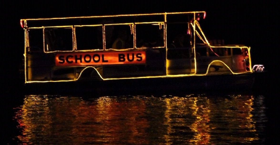 Boat decorated with lights shaped like a school bus at night.
