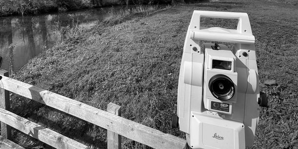 Leica surveying equipment set up near a wooden fence by a stream.