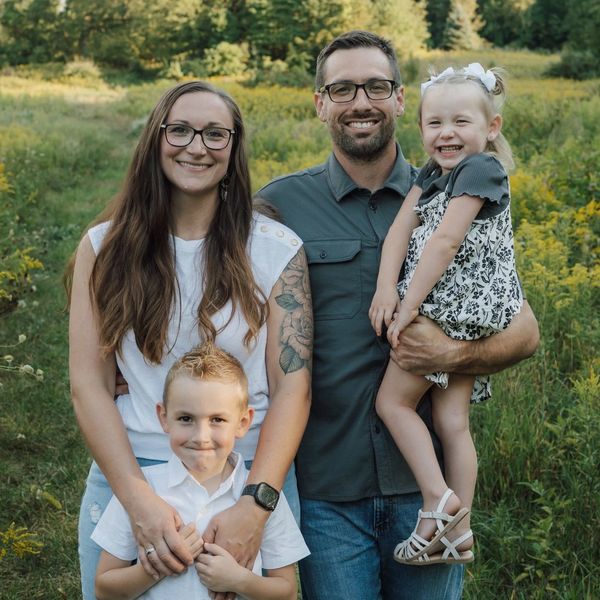 Happy family of four posing outdoors in a green field.