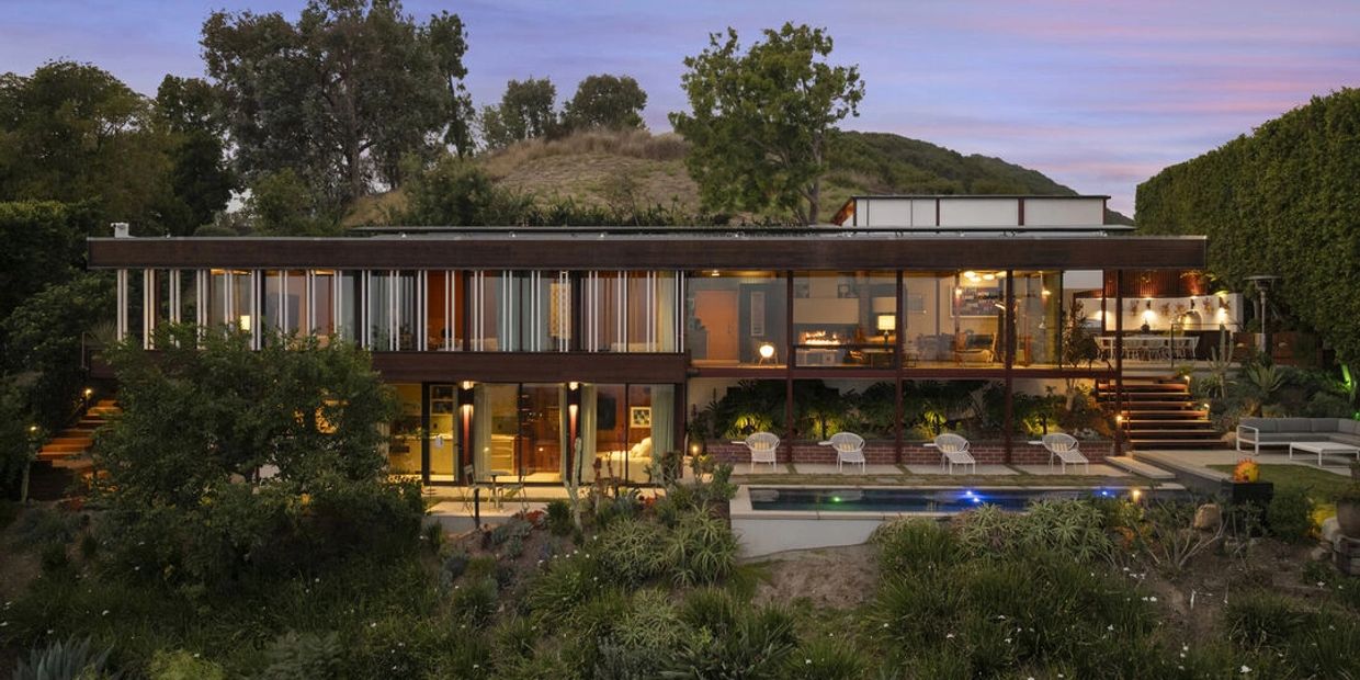 Modern glass house at dusk with pool and outdoor seating.