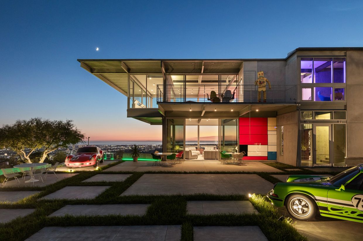 Modern house with two vintage sports cars at dusk.