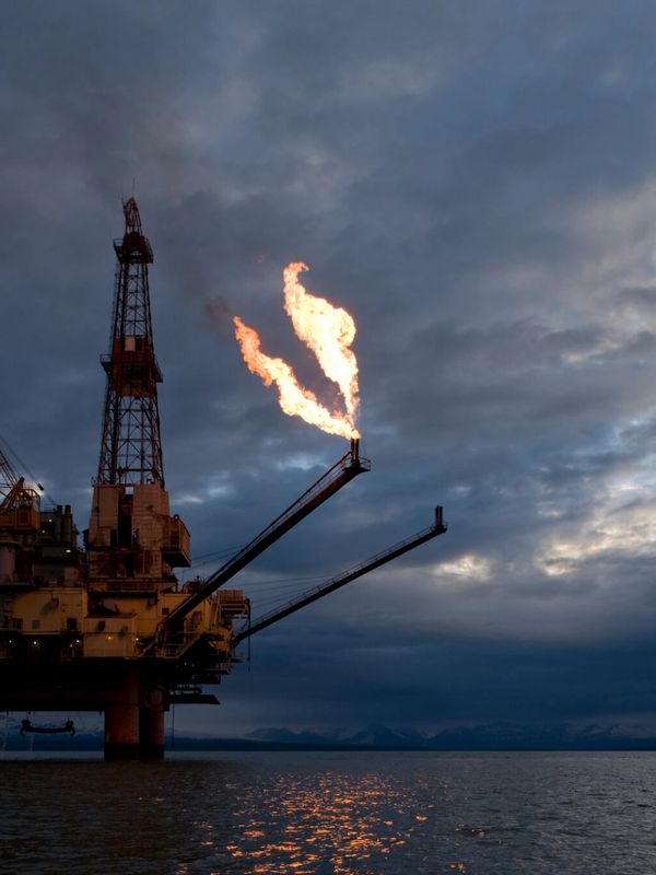 Offshore oil rig flaring gas under a cloudy sky at dusk.