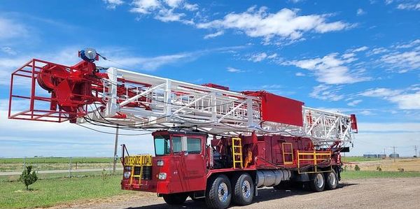 Large red and white drilling rig truck parked on a gravel road under a blue sky.