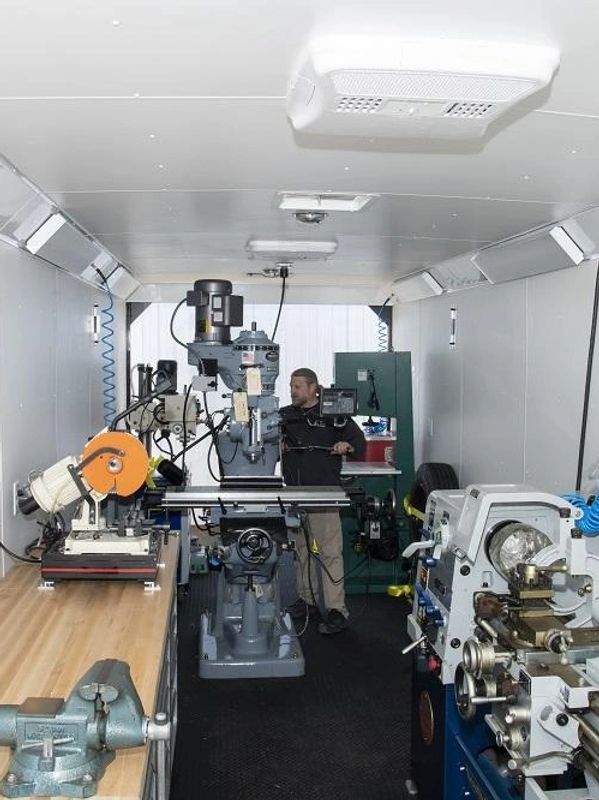 Inside a mobile workshop with various machining tools and a person operating one at the back.