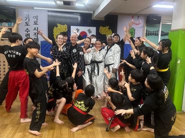 Martial arts group celebrating together in a dojo with a South Korean flag backdrop.
