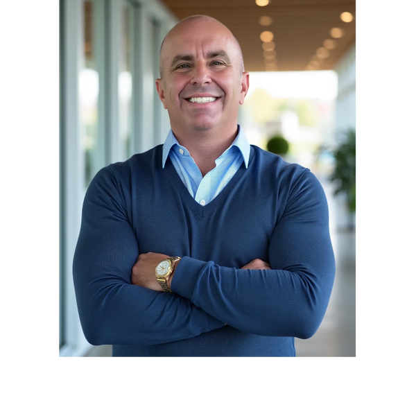 Smiling man in a blue sweater with arms crossed, standing indoors.