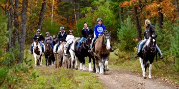 Group of people horseback riding through a forest trail in autumn.