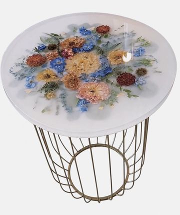 Round table with colorful dried flowers embedded in a clear resin top and gold metal base.