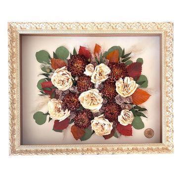 Framed arrangement of dried roses and autumn leaves with a decorative border.
