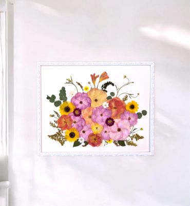 Framed floral artwork with vibrant pink, yellow, and orange flowers on a white wall.