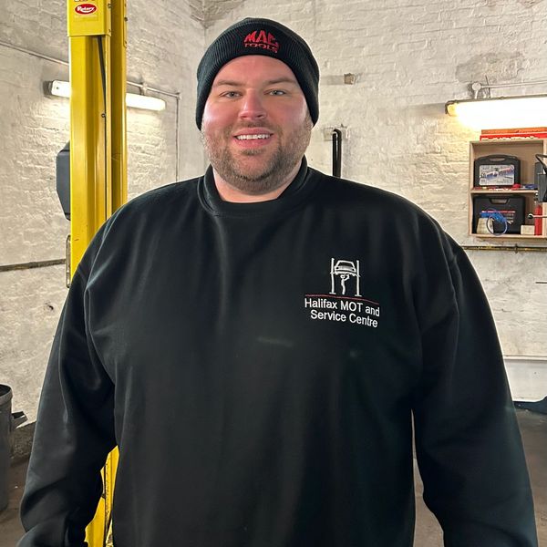 Smiling mechanic in black Halifax MOT and Service Centre sweatshirt and beanie.