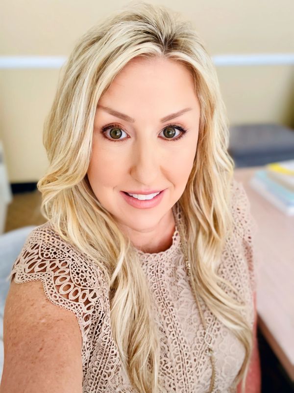 Smiling woman with long blonde hair and a lace top.