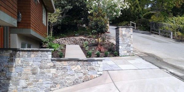 Stone retaining walls and a paved walkway near a house.