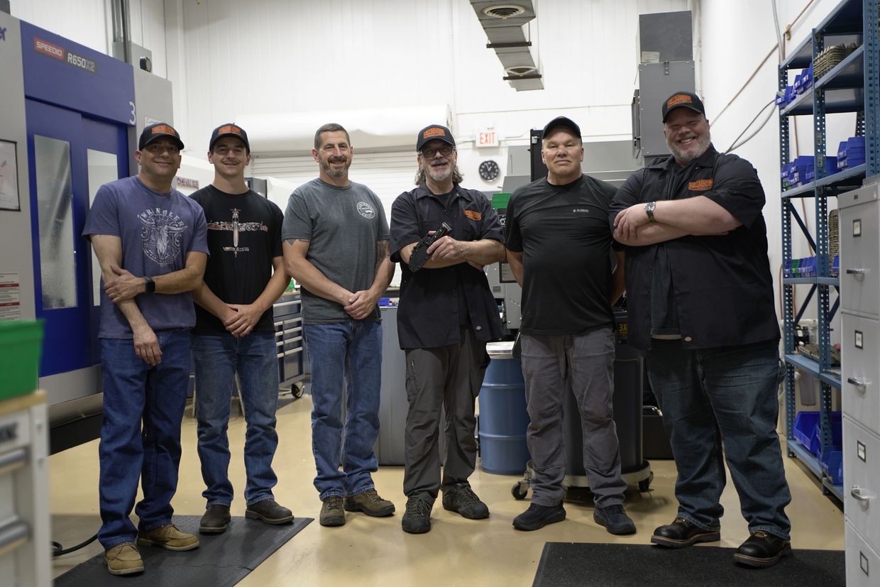 Six men standing in a workshop, smiling and posing for the photo.