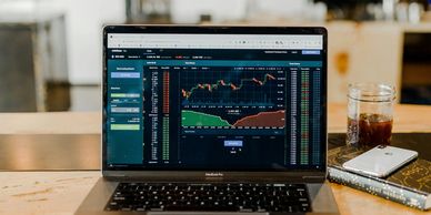 Laptop displaying cryptocurrency trading charts on a wooden table.