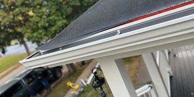 Close-up of a house gutter and roof edge with a blurred background of a vehicle and yard.