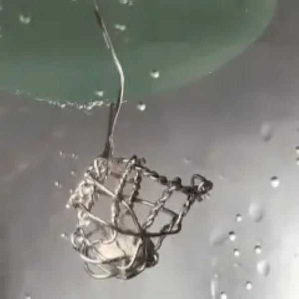 Close-up of a small wire basket holding a white object, suspended by a thin wire.